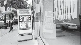  ?? STEVEN SENNE/AP ?? A passerby walks past a storefront with closing signs Sept. 2 in Boston.