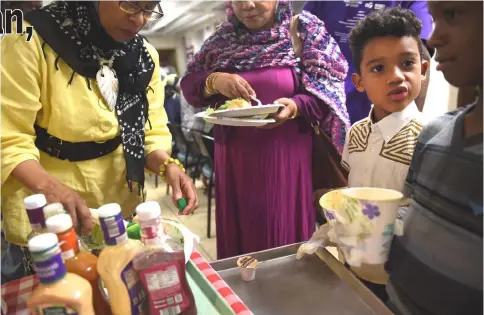  ??  ?? Khokhar, seven, in the white button-down shirt, helps serve food after a prayer service at the end of the day.