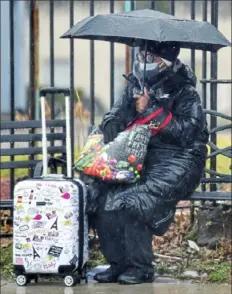  ?? Pittsburgh Post-Gazette ?? Sheltered under an umbrella, Sharon Griffin, of the Hill District, waits for a bus in the pouring rain Thursday along Bedford Avenue in the Hill District.