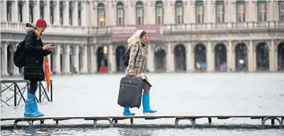  ??  ?? DELUGE: People use trestle bridges to walk across a flooded St Mark’s Square in the heart of historic Venice