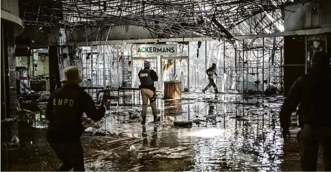  ?? Marco Longari/AFP ?? Policiais perseguem suspeito de participar de saques em shopping destruído em Vosloorus, na província de Gauteng, em meio a onda de violência na África do Sul