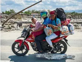  ??  ?? Desperate times: A quake-affected family riding with their belongings through a devastated area in Palu. — AFP