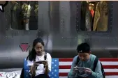  ?? — AP ?? Shoppers sit on a bench decorated with US flag browsing their smartphone­s outside a fashion boutique selling US brand clothing at a popular shopping mall in Beijing on Monday.