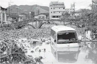  ?? REUTERS ?? A broken bridge is seen in the back, as an overturned vehicle and a partially submerged bus are pictured in floodwater­s caused by torrential rain in Hitoyoshi, Kumamoto Prefecture, southweste­rn Japan on Wednesday.