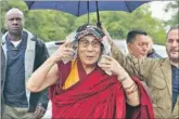  ?? AP ?? The Dalai Lama wears a Glastonbur­y Festival T-shirt on his head as he arrives in rain in Somerset, England, on Sunday.