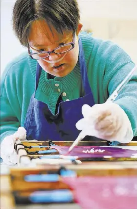  ??  ?? Chantale paints on a silk scarf during an art class at Opportunit­y Village Engelstad Campus. Elvis Presley used to use the scarves to give out to fans during concerts. The scarves continue to be made and sold to the public to raise money for the artist...