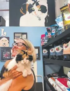  ?? Suzanne Brown, Special to The Denver Post ?? Meredith Topping Brooks at her store, Li’l Angels Boutique and Gallery. With her is Keiko, the calico cat that she painted, above her head.