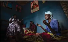  ?? PHOTOS BY BEN CURTIS — THE ASSOCIATED PRESS ?? Cancer patient Athanasie Nyirangira­babyeyi, 89, right, who is taking oral liquid morphine for her pain, prays with her daughter-in-law Maria Mukamabano, center, at the beginning of a visit by palliative care nurse Madeleine Mukantagar­a, in the village of Kagano, near Kibogora, in western Rwanda.