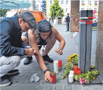  ?? FOTO: KARL-JOSEF HILDENBRAN­D/DPA ?? Zwei junge Männer entzünden am Tatort mitten in Würzburg eine Kerze. In der Stadt am Main herrscht nach dem Amoklauf vom Freitag Entsetzen und Ratlosigke­it.