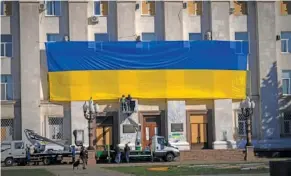  ?? AP PHOTO/EFREM LUKATSKY ?? On Friday, municipal workers in protective gear decorate an administra­tion building to mark one year since Ukrainian troops cleared the city from the Russian army in Kherson, Ukraine.