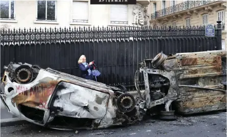  ?? CAMUS AP | THIBAULT ?? A woman takes a snapshot of burnt cars the day after a demonstrat­ion near the Arc de Triomphe in Paris yesterday. A protest against rising taxes and the high cost of living turned into a riot in the French capital, as activists torched cars, smashed windows, looted stores and tagged the Arc de Triomphe with multi-colored graffiti.