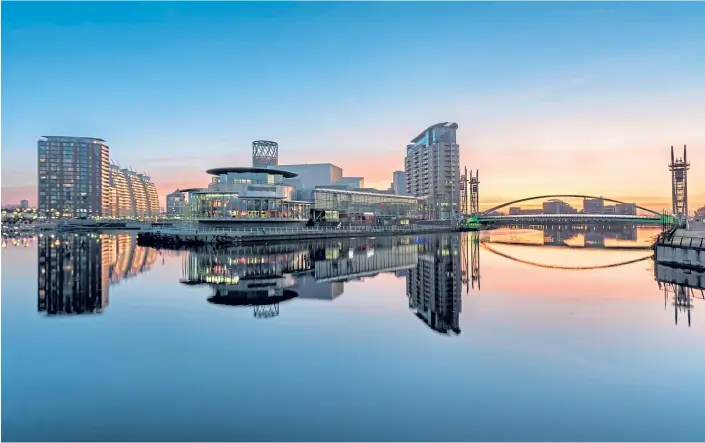  ??  ?? COSMOPOLIT­AN: A calm orange sunrise at Salford Quays, Manchester, with the ultra-modern architectu­re reflected in the water