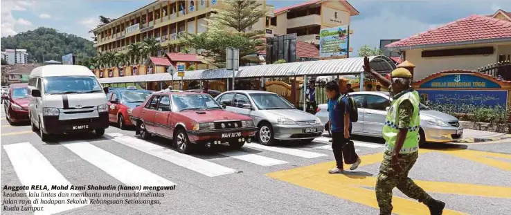  ??  ?? Anggota RELA, Mohd Azmi Shahudin (kanan) mengawal keadaan lalu lintas dan membantu murid-murid melintas jalan raya di hadapan Sekolah Kebangsaan Setiawangs­a, Kuala Lumpur.