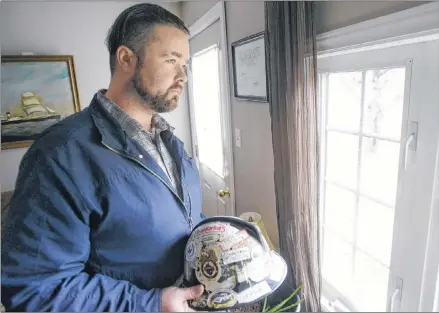  ?? MITCH MACDONALD/THE GUARDIAN ?? John Holmes holds his old hardhat while looking out the window of his Murray Harbour home. Holmes wants to raise awareness about mental health and career re-training supports offered in P.E.I. to former oil patch workers struggling with the industry’s decline.