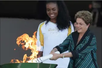  ??  ?? Brazil’s President Dilma Rousseff lights the Olympic flame as Brazilian volleyball player Fabiana Claudino looks on during the lighting ceremony at Planalto presidenti­al palace Tuesday in Brasilia, Brazil. The start of the torch relay comes just a week...