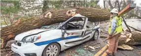  ?? MICHAEL BRYANT THE PHILADELPH­IA INQUIRER VIA AP ?? An electrical worker for INTREN walks by a damaged vehicle in Bryn Mawr, Pa., on Sunday.