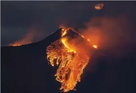  ??  ?? The moon is partially seen in the sky as lava flows from the Mount Etna volcano Photograph: Salvatore Allegra/AP