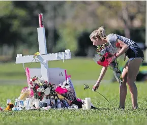 ?? GERALD HERBERT / THE ASSOCIATED PRESS ?? A woman places flowers Friday at one of 17 crosses placed for the victims of the shooting at Marjory Stoneman Douglas High School in Florida.