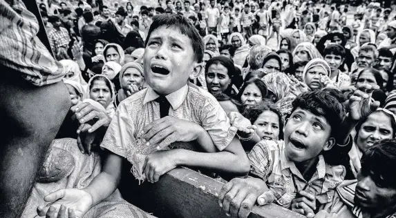  ??  ?? > A Rohingya refugee boy desperate for aid cries as he climbs on a truck distributi­ng aid for a local NGO near the Balukali refugee camp in Cox’s Bazar, Bangladesh