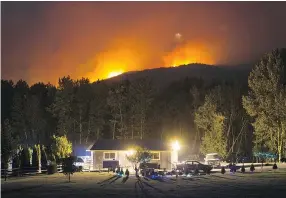  ??  ?? A wildfire burns on a mountain behind a home in Cache Creek overnight Friday. More than 3,000 residents have been evacuated from their homes in central British Columbia.