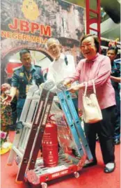  ??  ?? Senior citizens Francis Leong and wife Josephine, both 75, using a ladder which doubles up as a trolley, an invention by the Malacca Fire and Rescue Department, to cart a fire extinguish­er at the fire prevention and innovation campaign in Kuantan...