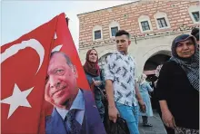  ?? LEFTERIS PITARAKIS THE ASSOCIATED PRESS ?? As Turkey's finance chief tried to reassure internatio­nal investors during a conference call Thursday, shoppers pass by a vendor selling flags.