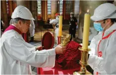  ??  ?? Patrick Chauvet, Pfarrer der Kathedrale, hält die Dornenkron­e, die Jesus getragen haben soll. Der Helm schützt vor herabfalle­nden Teilen, der Mundschutz vor Corona.
