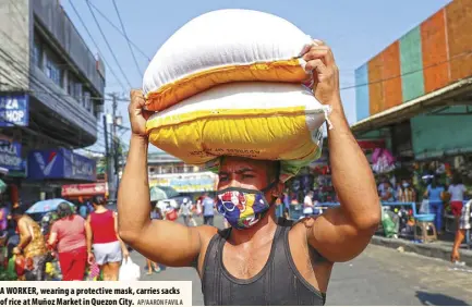  ?? AP/AARON FAVILA ?? A WORKER, wearing a protective mask, carries sacks of rice at Muñoz Market in Quezon City.