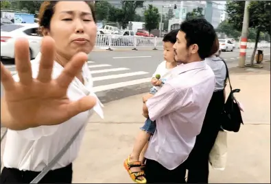  ?? AP/GERRY SHIH ?? Hua Xiaoqin (left), sister of Chinese labor activist Hua Haifeng, tries to block a reporter from approachin­g him as Haifeng, carrying his son, leaves a police station Wednesday in Ganzhou in southern China’s Jiangxi province.