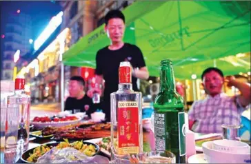  ?? HECTOR RETAMAL/AFP ?? A bottle of baijiu liquor is seen on a table while people enjoy dinner at an eatery in Luzhou.