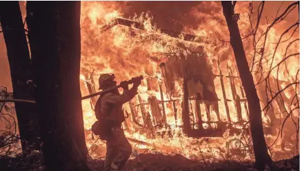  ??  ?? Firefighte­r Jose Corona sprays water as flames from the Camp Fire consume a home in Magalia, California, on Friday.