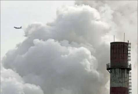  ?? Andy Wong/Associated Press ?? A passenger airliner flies past steam and white smoke emitted from China Huaneng Group's Beijing power plant. The coalfired plant was shut down last year as the Chinese convert to clean energy like thermal power.