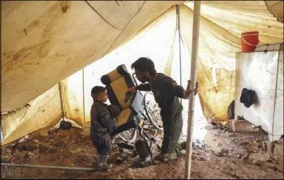  ??  ?? معاق حرب سوري مع طفله يحمل كرسيه المتحرك في مخيم للاجئين قرب الحدود التركية