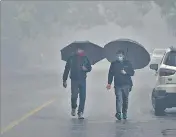  ?? AGENCIES ?? People walk with umbrellas amid light rain on a foggy winter morning, in New Delhi on Wednesday.