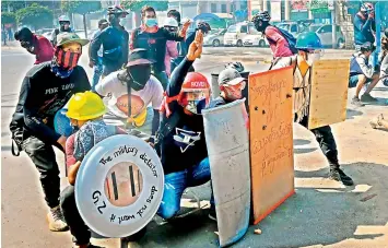  ?? AFP ?? Protesters take cover behind homemade shields during a demonstrat­ion against the military coup in Yangon on Sunday. —