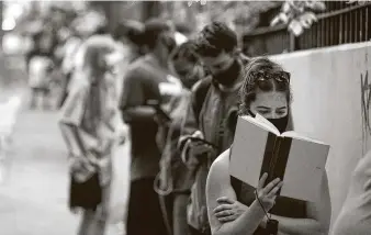  ?? John Bazemore / Associated Press ?? Kelsey Luker reads as she waits in line to vote Tuesday in Atlanta. Luker said she had been in line for almost two hours. Voters around Georgia experience­d long delays and equipment problems.