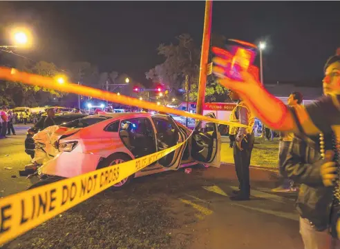  ?? Picture: AP ?? NARROW ESCAPE: People walk by a wrecked car as police work at the scene where a pick-up truck ploughed into a crowd watching the Krewe of Endymion parade in New Orleans yesterday.