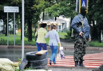  ?? Dominique Faget/AFP/Getty Images ?? An armed pro-Russian militant, member of the Vostok battalion, stands guard at a crosswalk as pedestrian­s cross a street in Donetsk. There are fewer people and cars on the streets as residents brace for the battle ahead between the militants holed up...