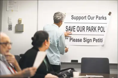  ?? Michael Cummo / Hearst Connecticu­t Media ?? Stamford resident Deborah Billington, of the Stamford Neighborho­od Coalition, hangs a sign supporting the parks police before the parks committee meeting Wednesday. The sign was taken down before the meeting, but Billington held it for the duration. Below left, parks and recreation co-chair Dennis Mahoney, R-20, speaks during the meeting. Below right, two people chat on a park bench in Cummings Beach Park in Stamford on Tuesday.