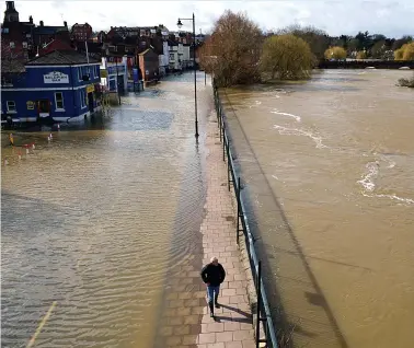  ??  ?? Pedestrian walks between flooded Shrewsbury street, left, and the River Severn, right, yesterday