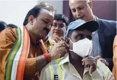  ?? — AFP ?? East Delhi Municipal Corporatio­n (EDMC) Mayor Bipin Bihari Singh (L) distribute­s N-95 anti-pollution mask to EDMC workers to help them breathe while at work, at a ceremony in New Delhi on Thursday.