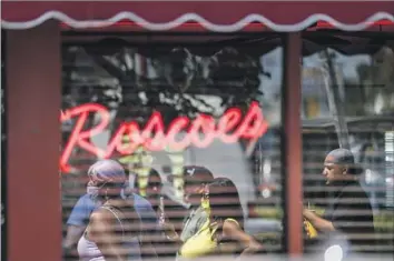  ?? Photograph­s by Robert Gauthier ?? COMMUNITY MEMBERS look on Tuesday as a news conference is held at the Roscoe’s House of Chicken & Waff les outlet where PnB Rock was fatally shot the previous day. The restaurant had few customers.