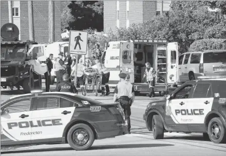  ?? CP PHOTO ?? Police officers and paramedics survey the area of a shooting in Fredericto­n, N.B. on Friday.