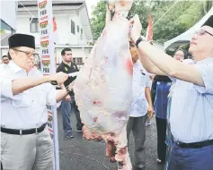 ??  ?? Abang Johari (left) and Fadillah slice the sacrificia­l meat to mark the occasion. — Photo by Chimon Upon