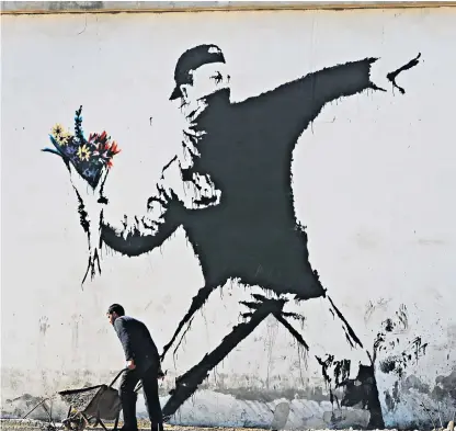  ??  ?? Banksy’s original Flower Thrower, which appeared on a wall in Jerusalem, shows a masked man throwing a bouquet in the name of peace