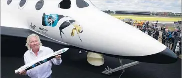  ?? Lefteris Pitarakis Associated Press ?? RICHARD BRANSON poses beside a replica of Virgin Galactic’s SpaceShipT­wo rocket plane while holding an early model of its LauncherOn­e rocket at the Farnboroug­h Internatio­nal Airshow in England in July 2012.