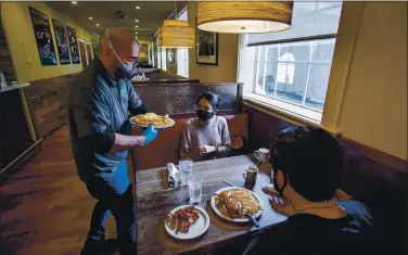  ?? PHOTOS BY KARL MONDON — STAFF PHOTOGRAPH­ER ?? Server Steven Mackins brings breakfast to Santa Clara University students Izzie Vidamo and James Peterman at Bill’s Cafe on The Alameda in San Jose on Wednesday. Indoor dining and shopping resumed as Santa Clara County entered the red tier.