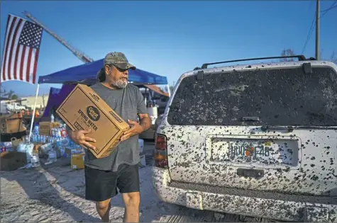  ?? Chang W. Lee/The New York Times ?? Thomas Ard, 55, heads to his car with a box of bottled water given to him by the United Cajun Navy, a volunteer rescue and relief organizati­on, in Lynn Haven, Fla., on Monday.