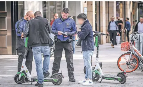  ?? FOTO: HANS-JUERGEN BAUER ?? Emre (2. v. l.) und Huijie (r.) bei der Kontrolle durch das Ordnungsam­t. Sie waren mit dem E-Scooter auf dem Bürgerstei­g unterwegs.