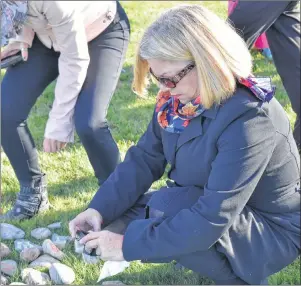  ?? NIKKI SULLIVAN/CAPE BRETON POST ?? Anne Marie Quirk of Sydney bends down to take a picture of the rock she will place at the bottom of the Survivor Tree in memory of her daughter Jenny Quirk, who died from suicide four years ago. Her name is painted on the rock her mother laid at the...